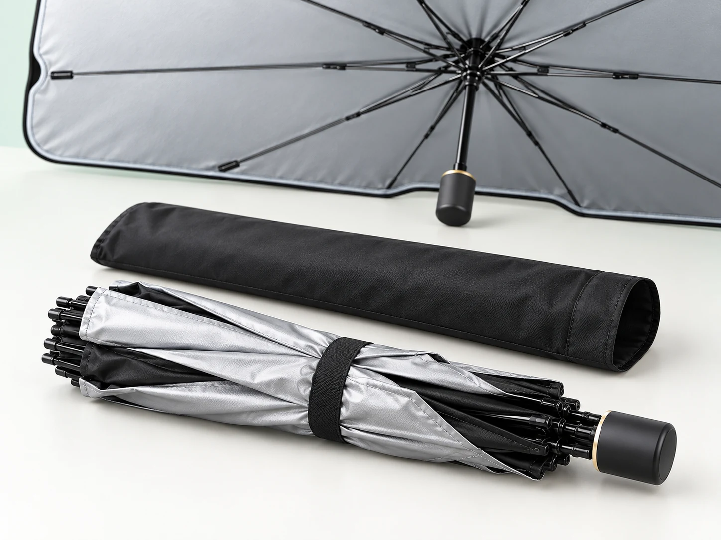 Illustration of a folded silver and black umbrella sunshade beside a storage sleeve